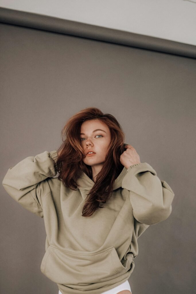 Portrait of a confident young woman in a trendy beige hoodie against a gray background.